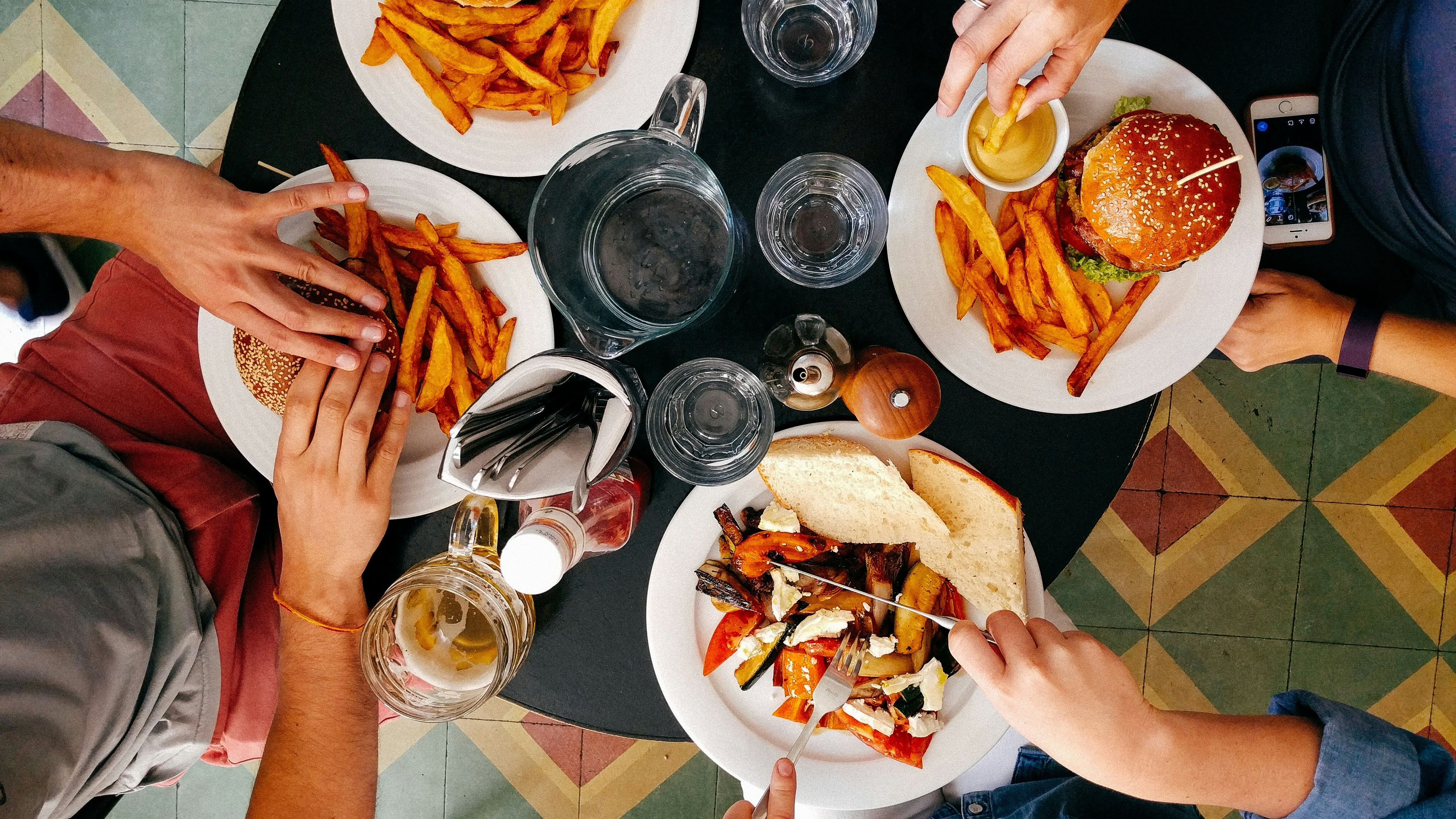 Top-down view of three people eating burgers, fries, and a sandwich at a restaurant table.