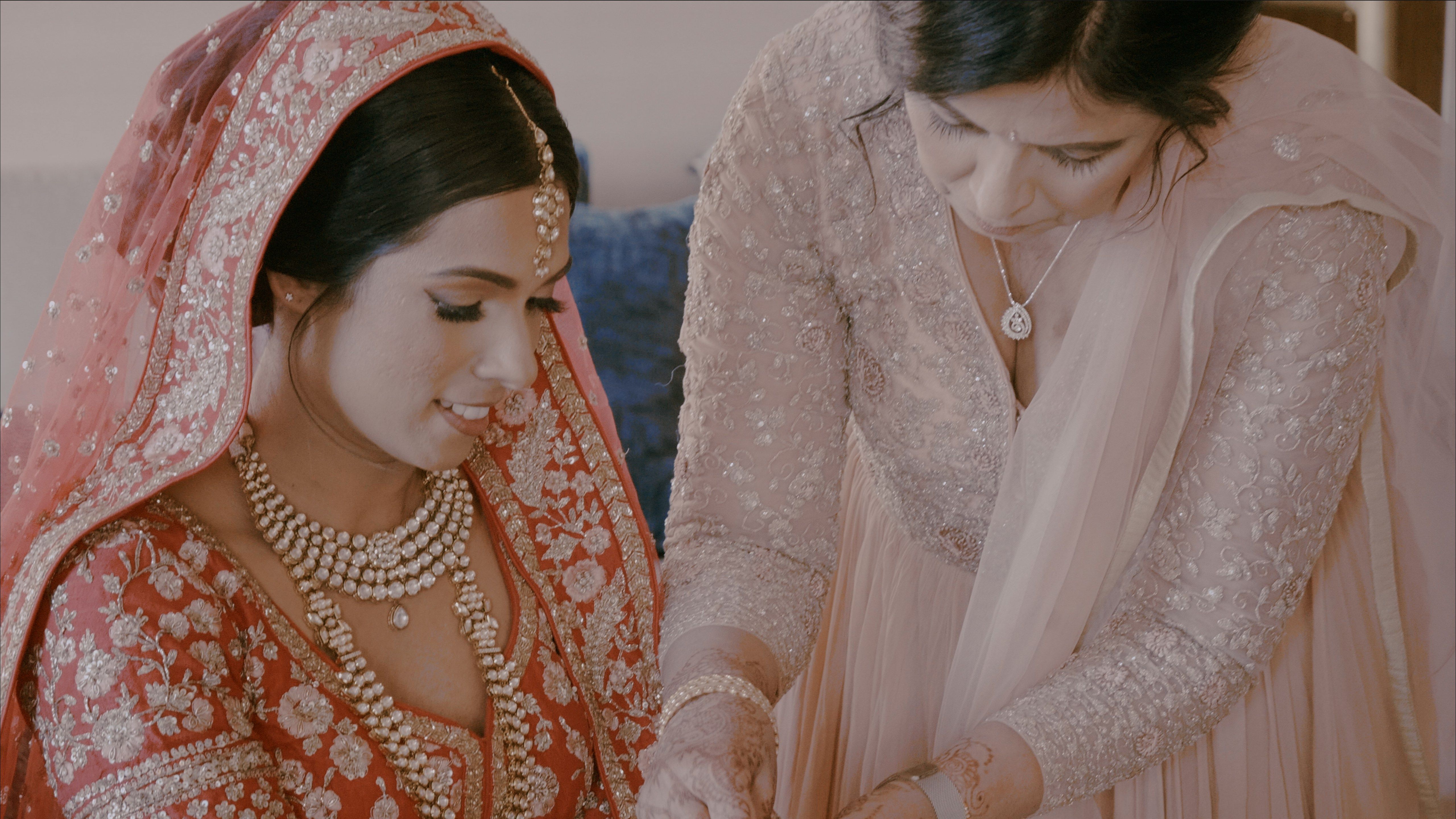 Bride in traditional red and gold attire with another woman helping her during a wedding ceremony