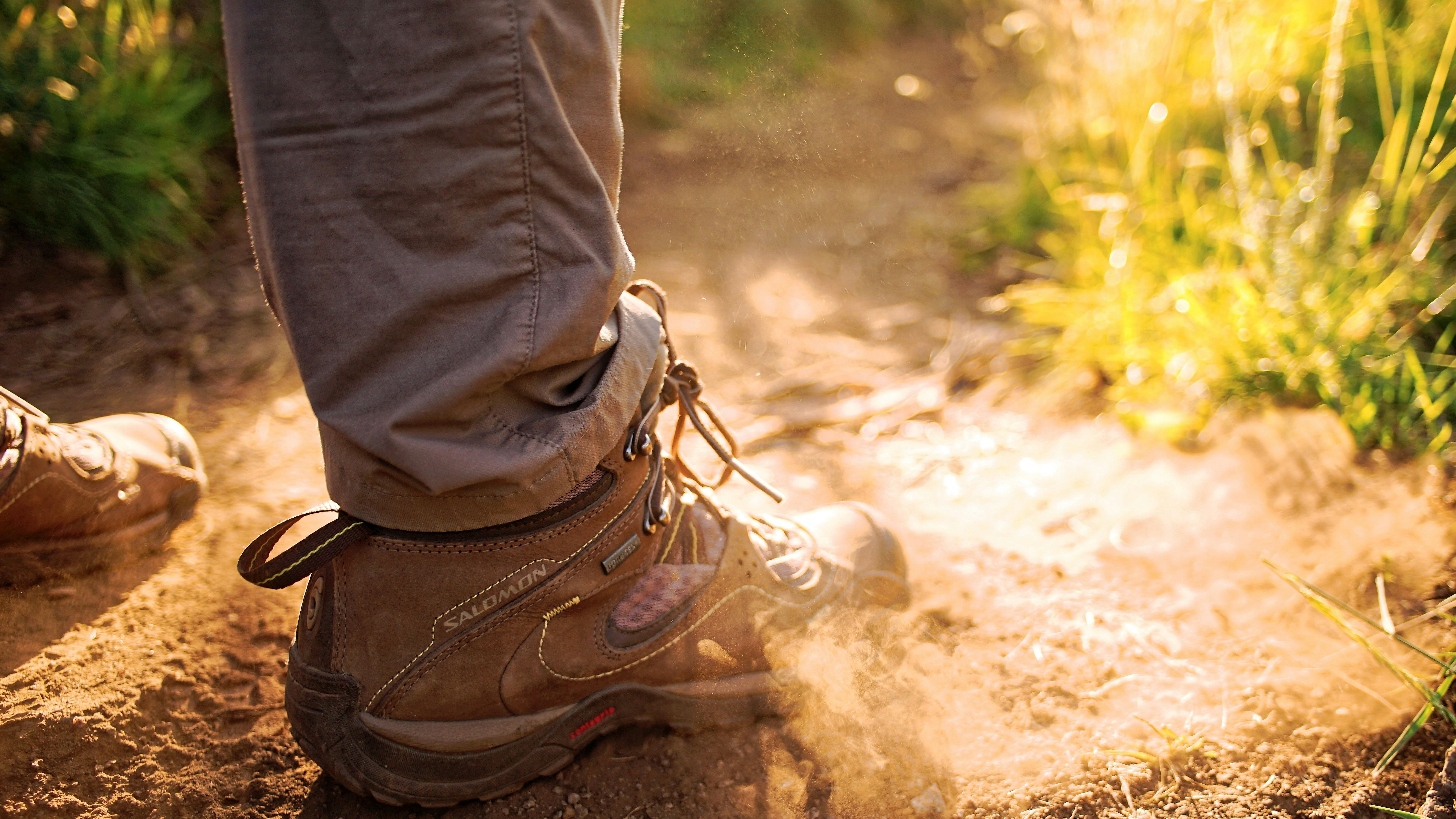 Close-up of a person wearing hiking boots walking on a dusty trail in sunlight