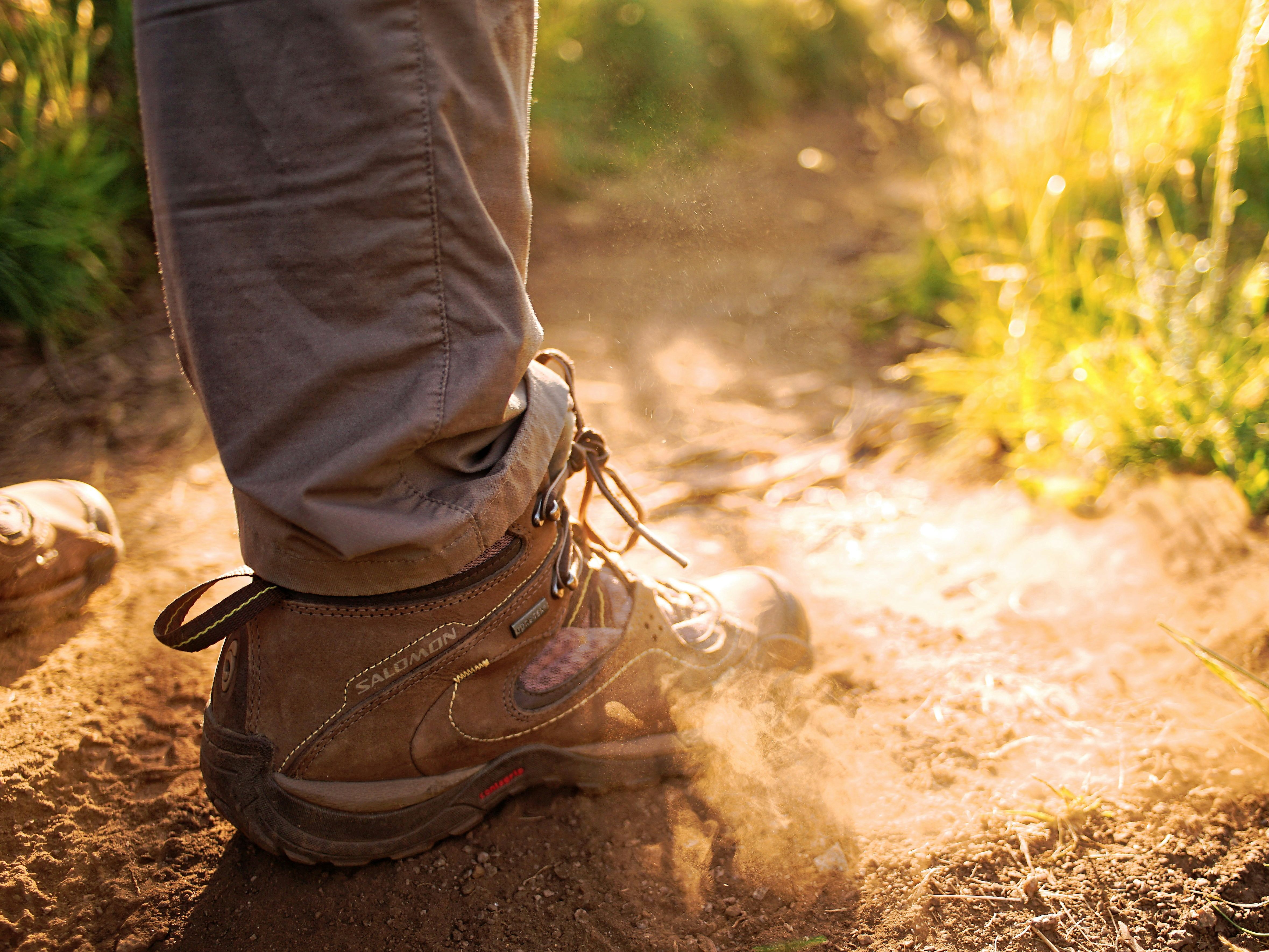 Close-up of a person wearing hiking boots walking on a dusty trail in sunlight