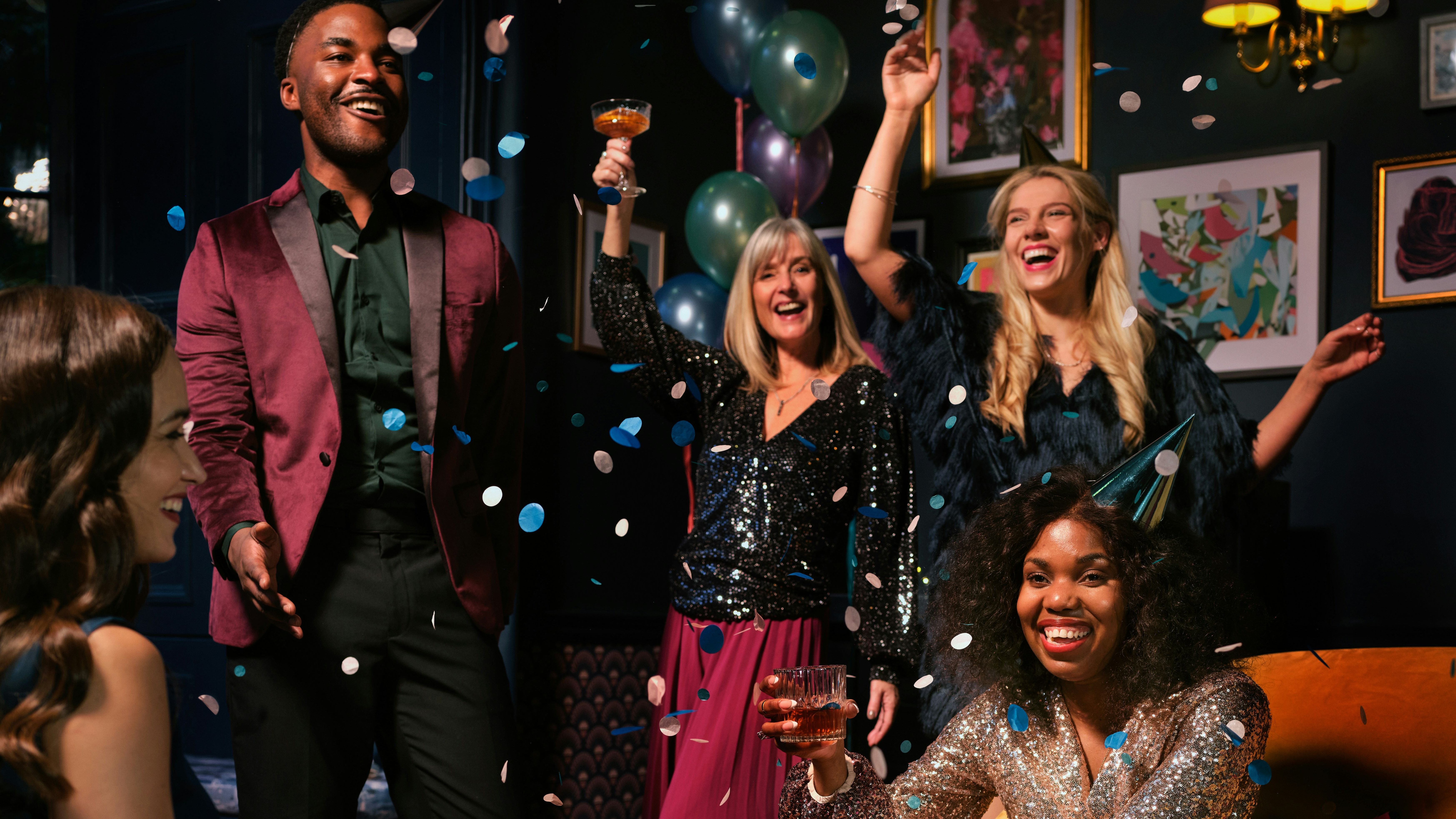 Group of friends celebrating at a party with confetti, drinks, and balloons in a festive indoor setting