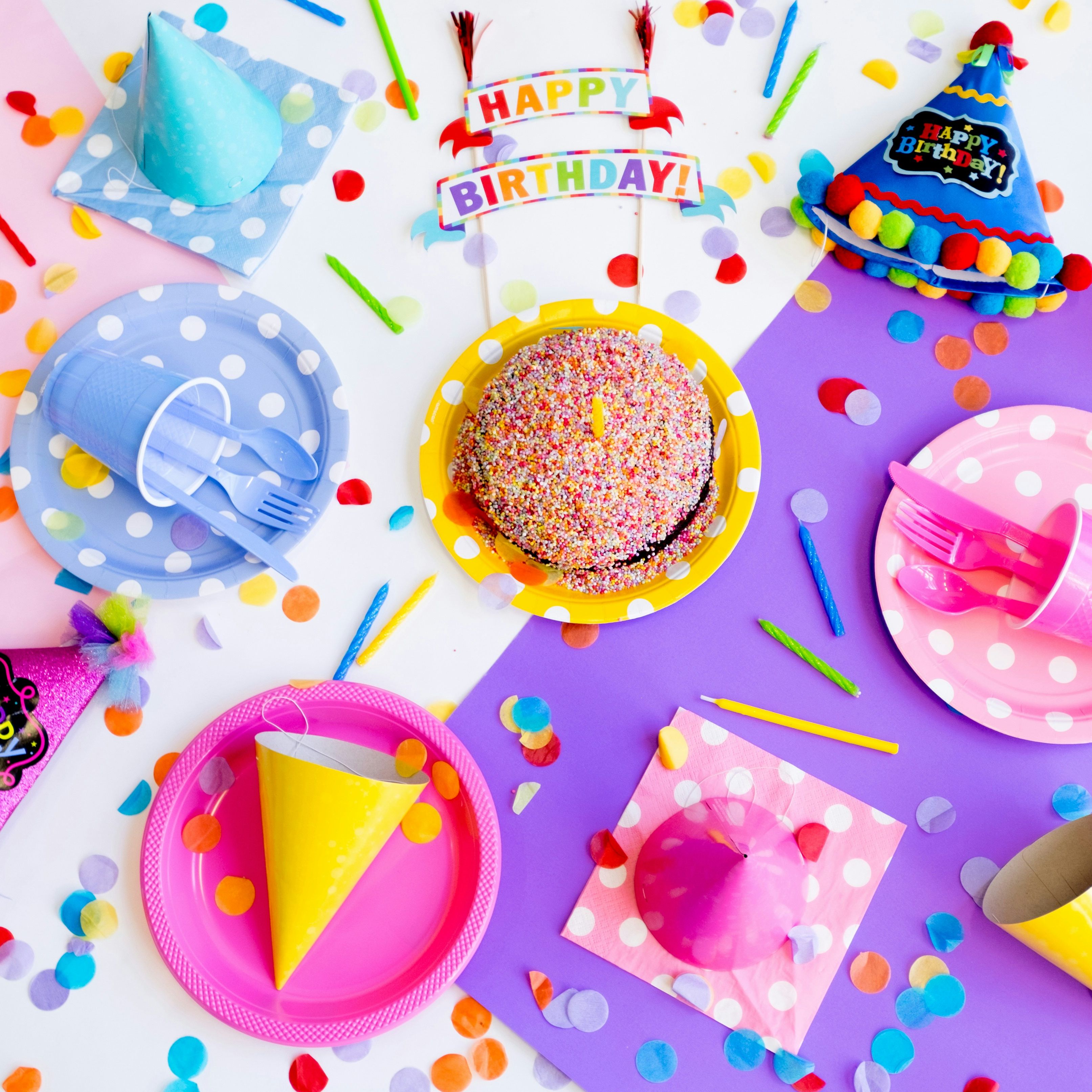 Colorful birthday party table top with hats, cake, confetti, and party supplies