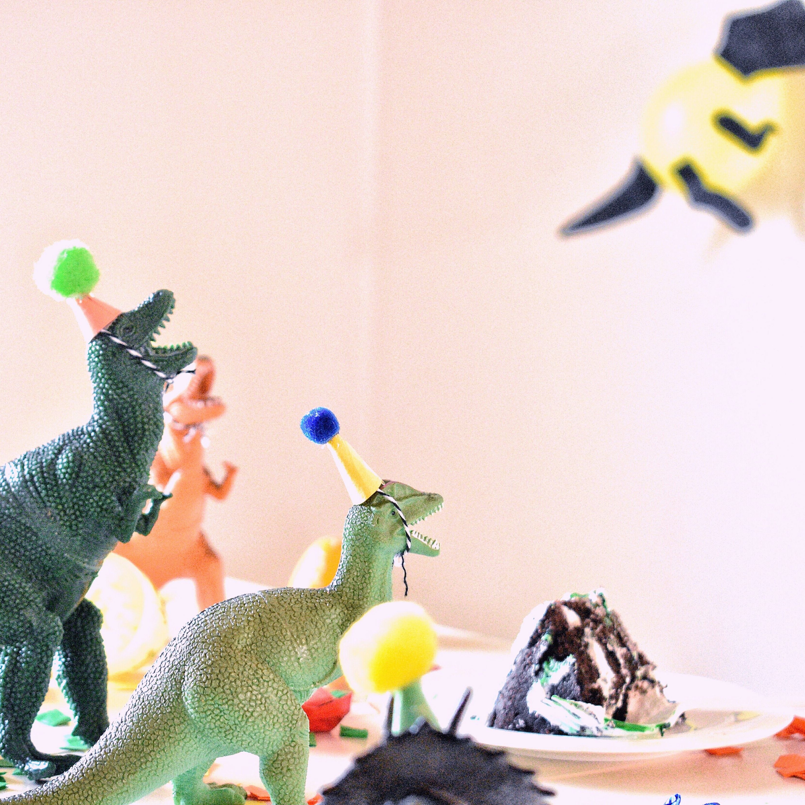 Toy dinosaurs wearing party hats at a table with cake and decorations