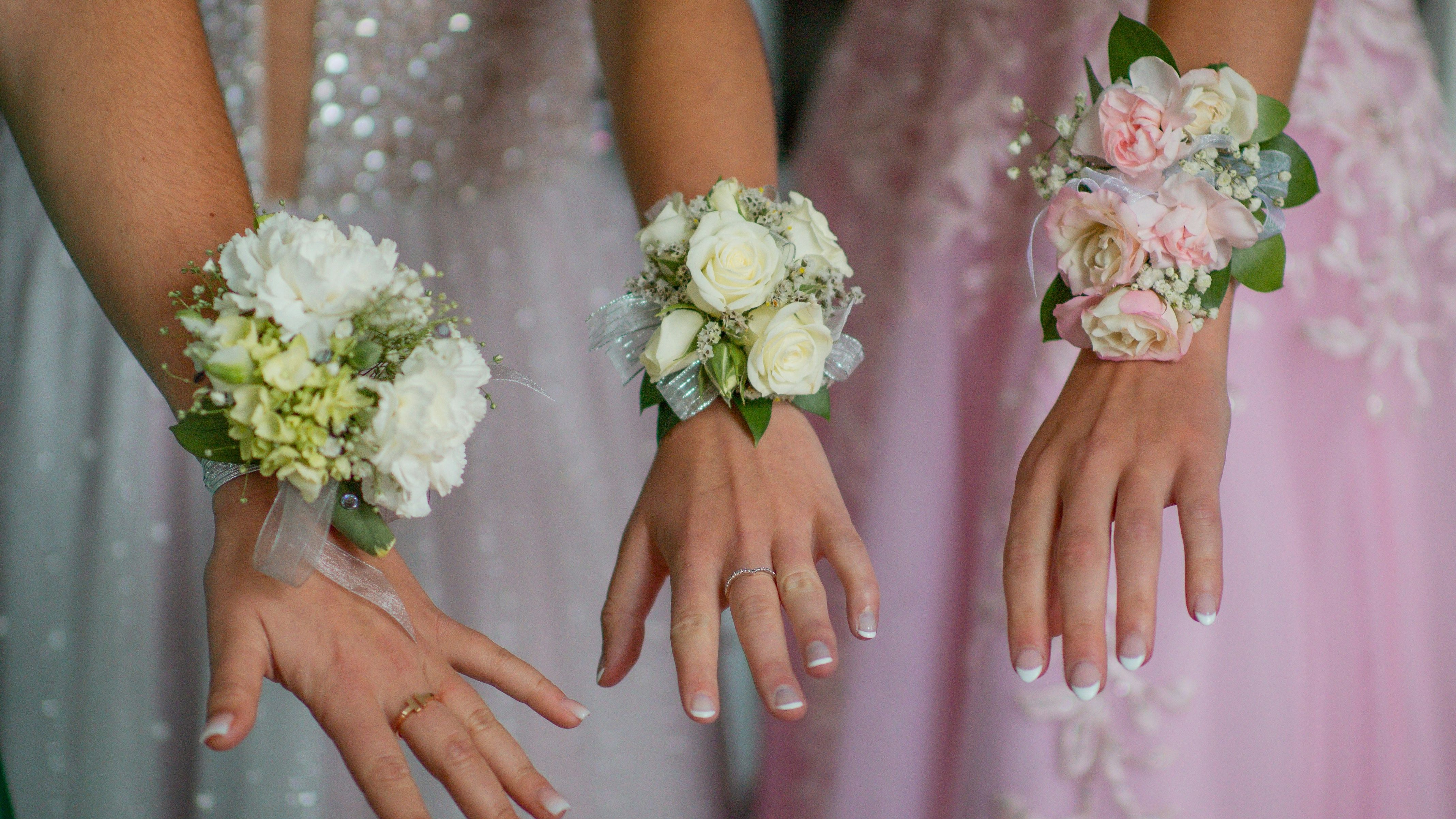 Close-up of three hands wearing floral corsages, dressed in formal gowns