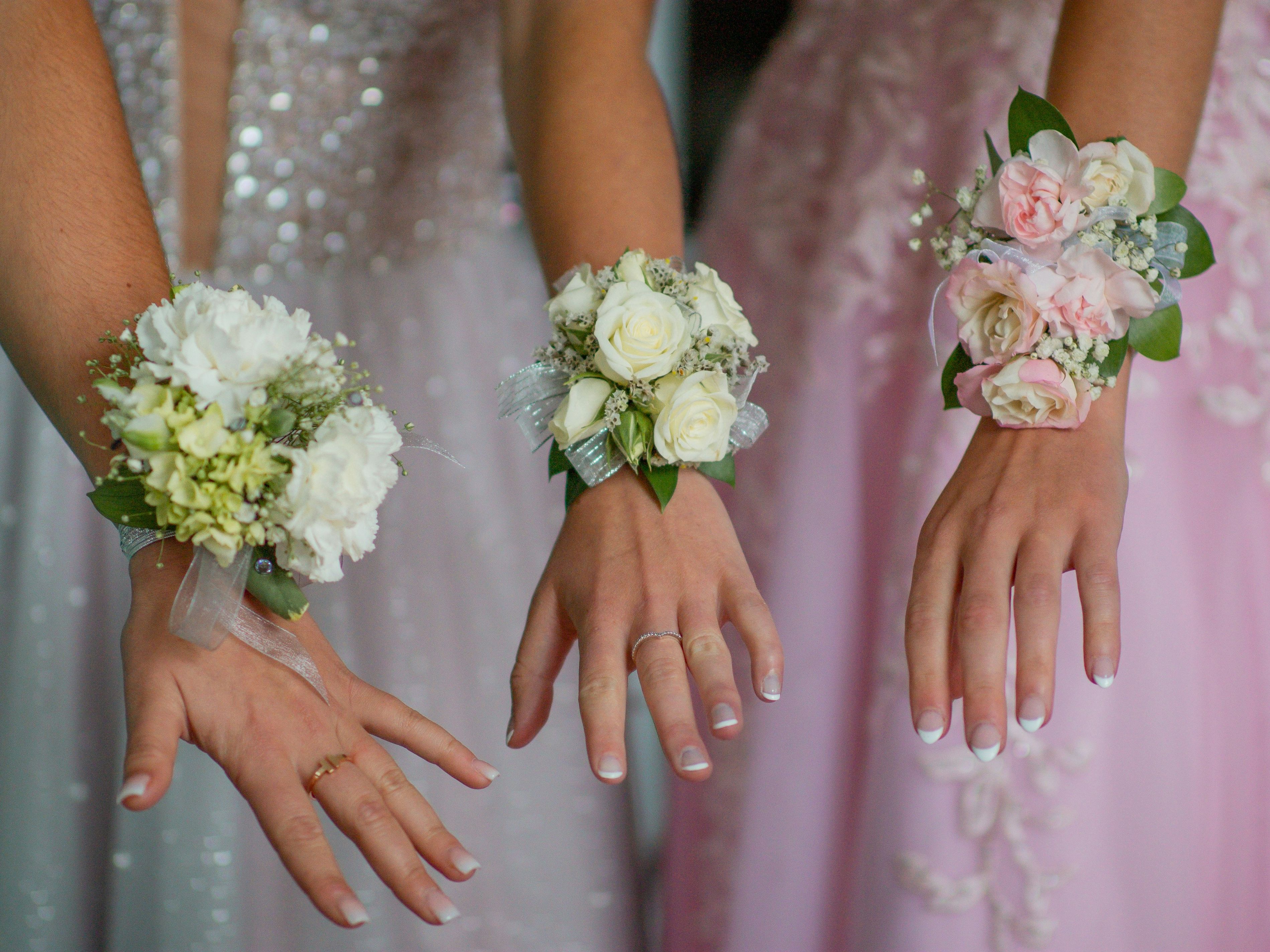 Close-up of three hands wearing floral corsages, dressed in formal gowns