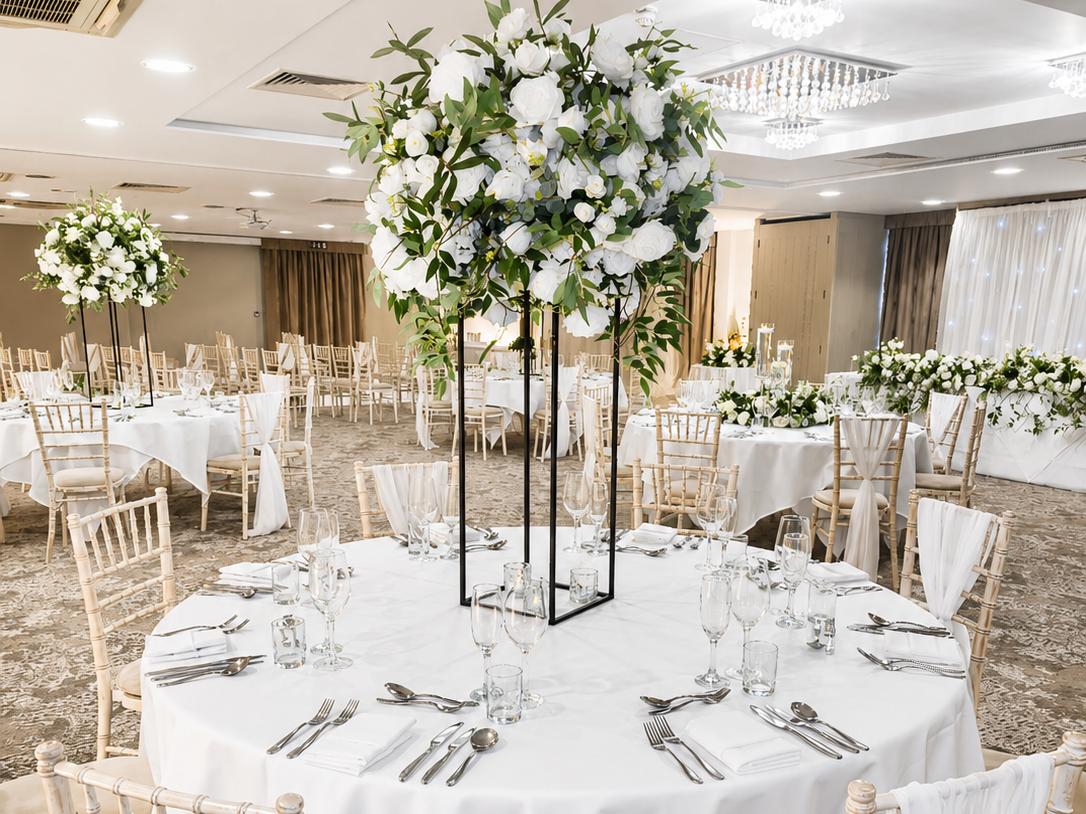 Elegant banquet hall with round tables decorated with white floral centerpieces and neatly arranged place settings.