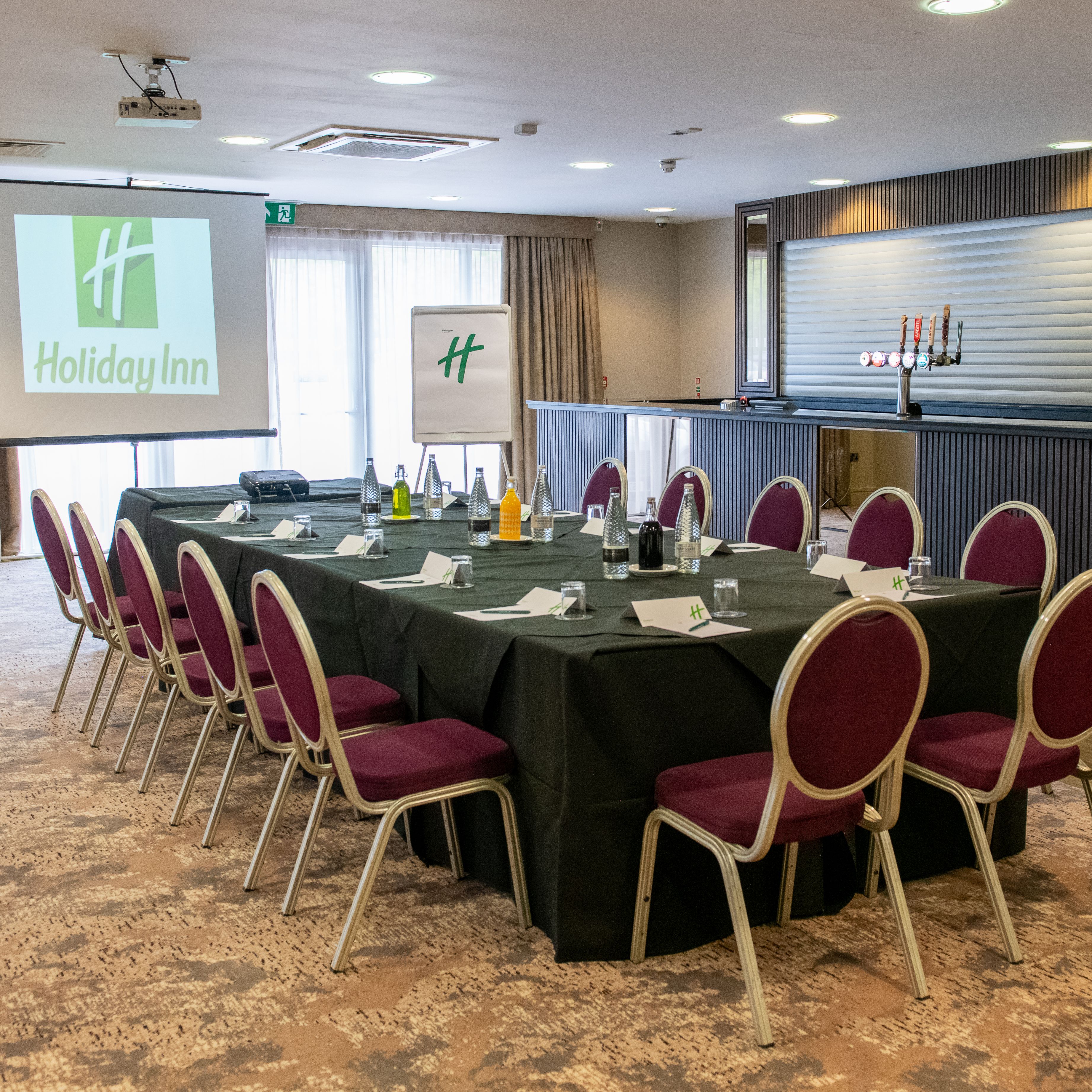 Conference room set up for a meeting at Holiday Inn with a large table, chairs, bottled water, and presentation screen.