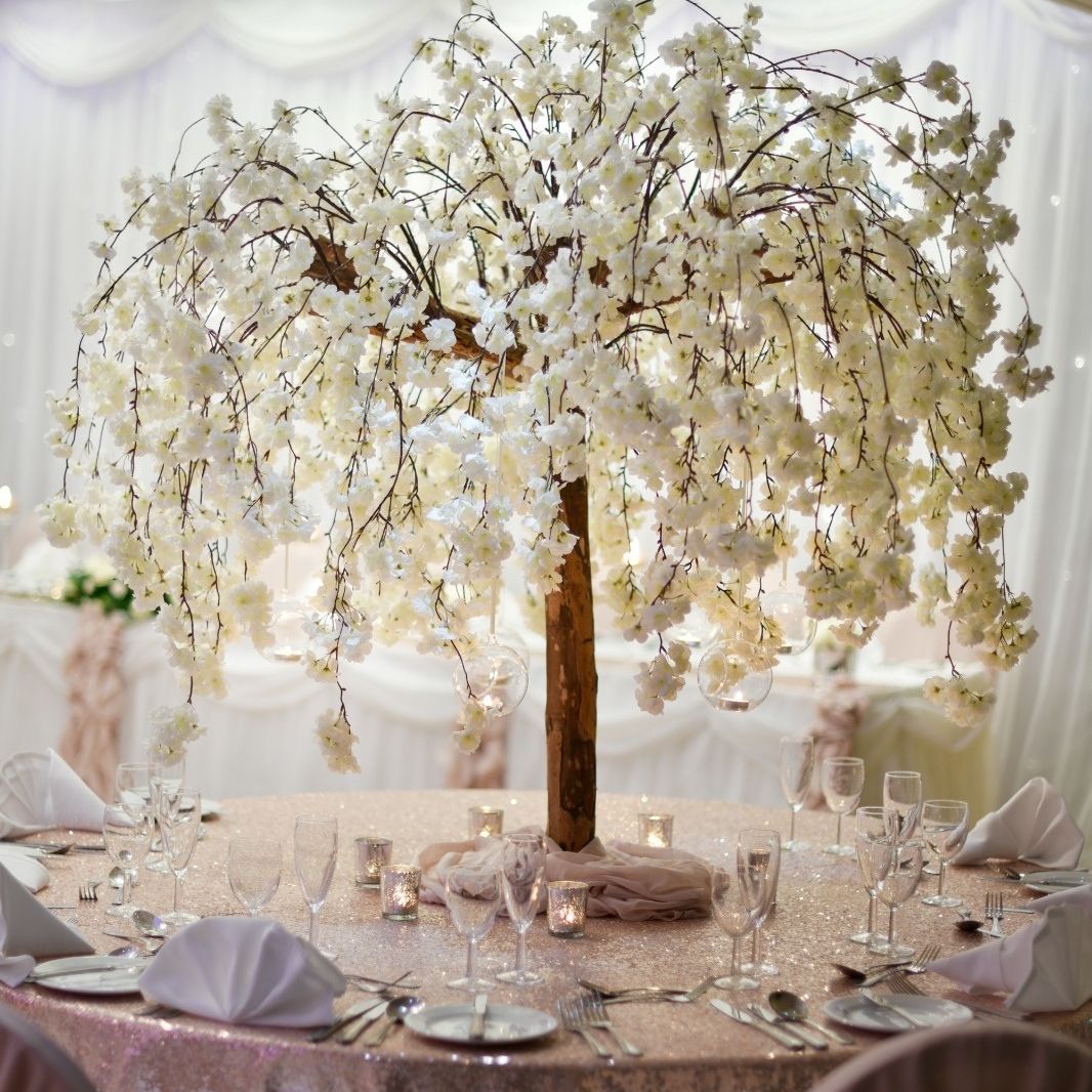 Elegant wedding table centerpiece with a large artificial white cherry blossom tree surrounded by table settings.