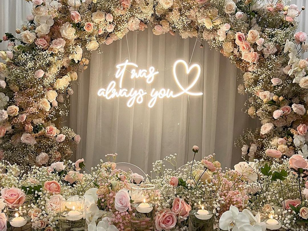 Romantic floral wedding arch with candles and a neon sign reading 'It was always you'