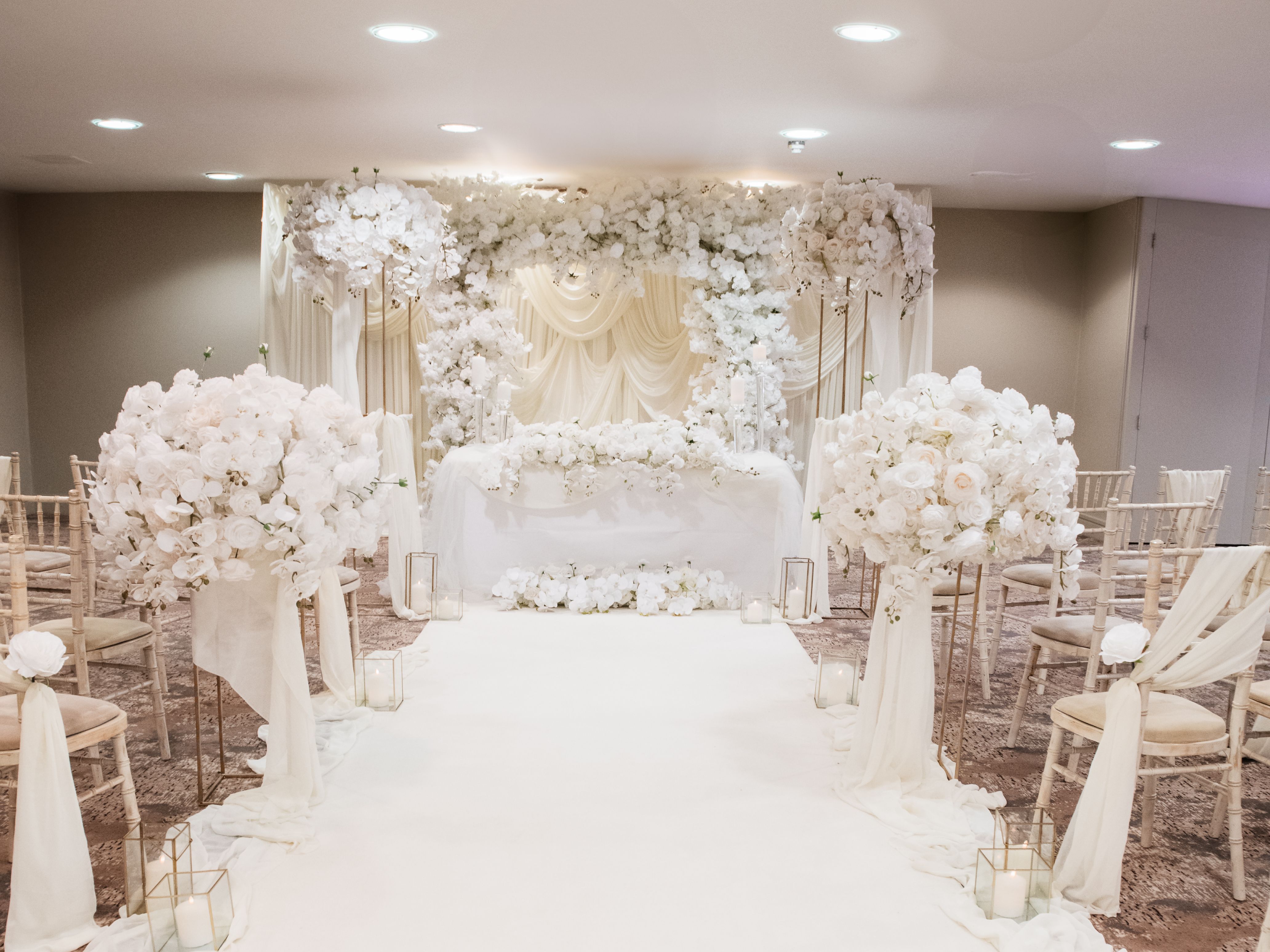 Elegant indoor wedding ceremony setup with white flowers and draped fabric