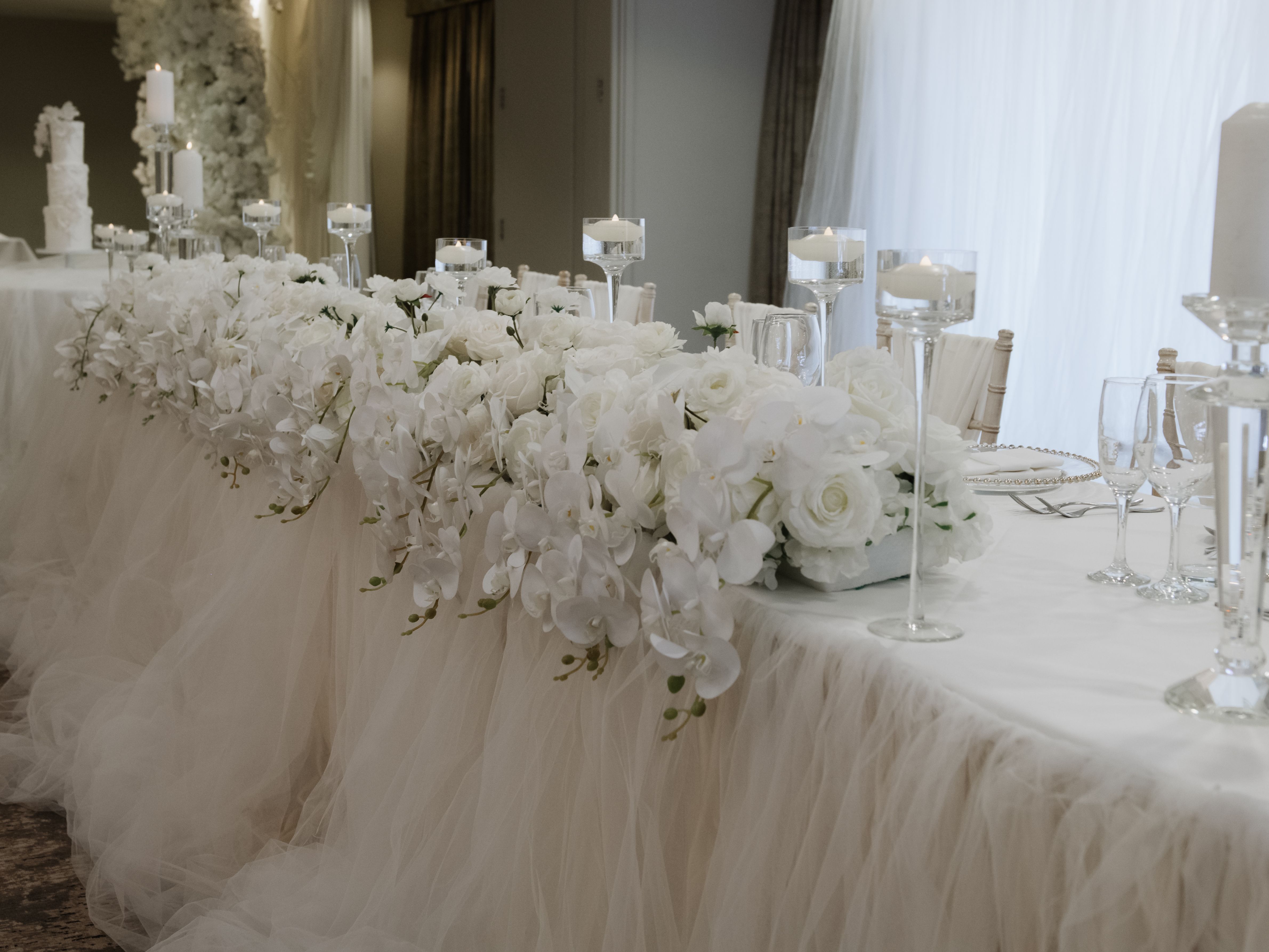 Elegant wedding table decorated with white flowers, candles, and tulle
