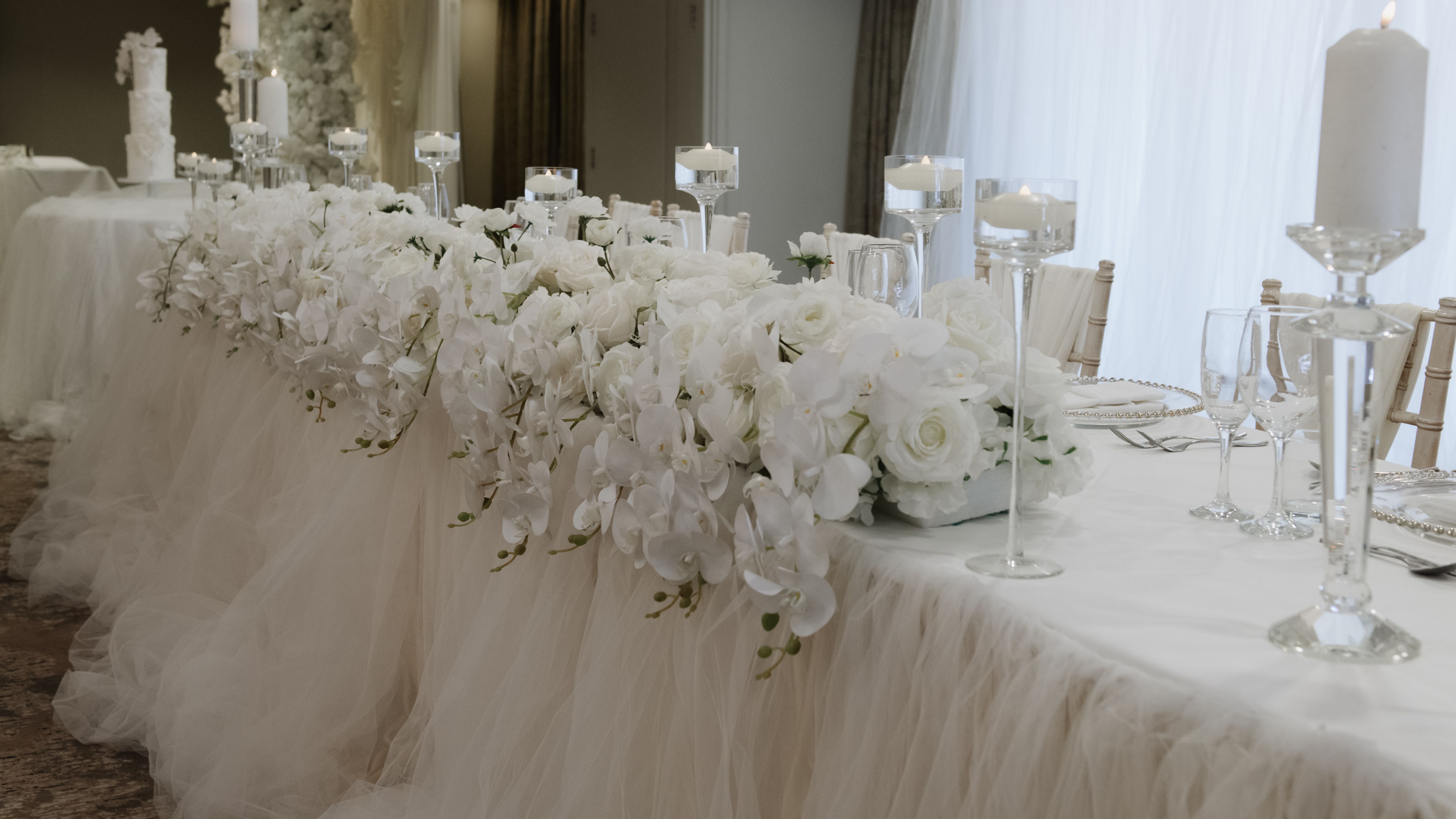 Elegant wedding table decorated with white flowers, candles, and tulle