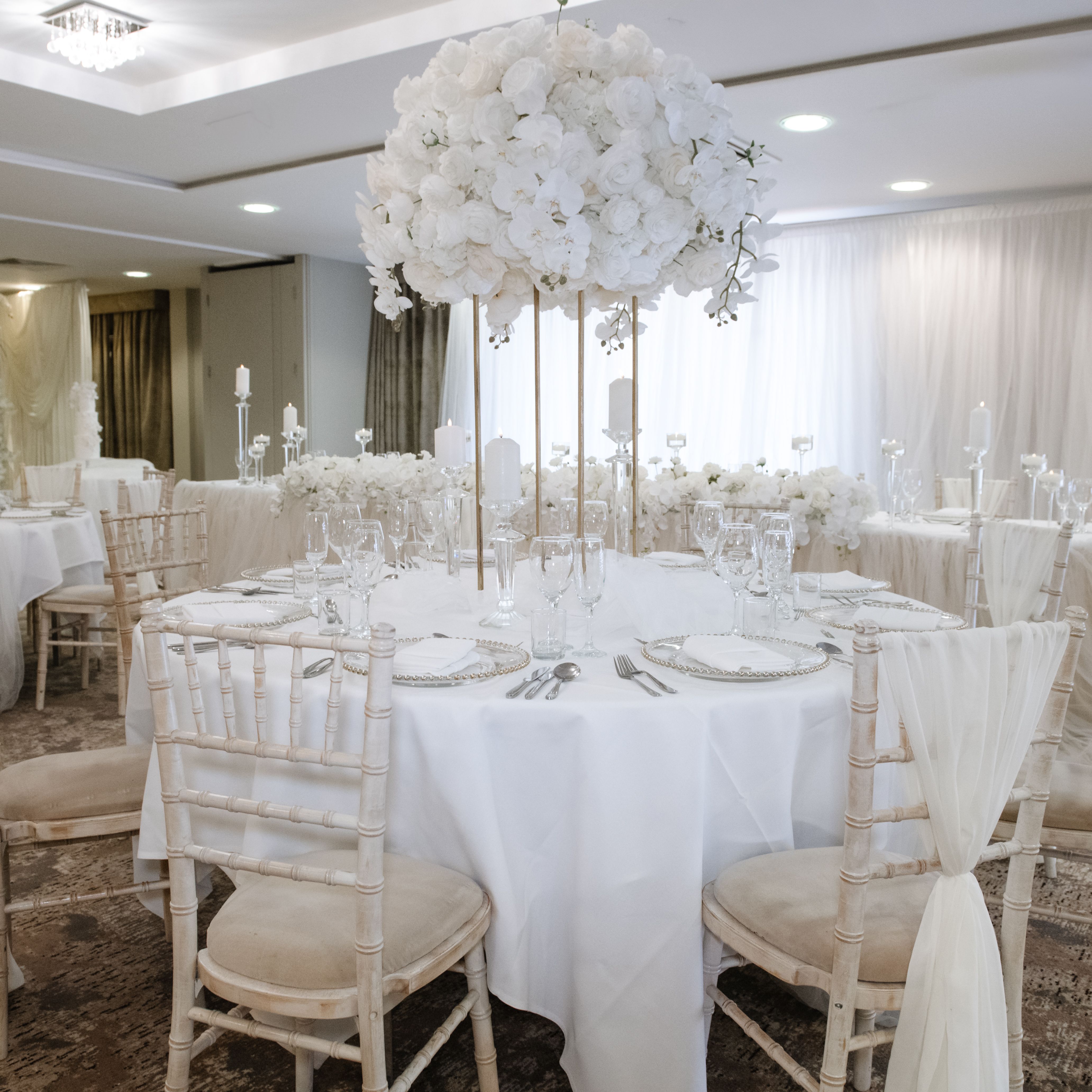 Elegant wedding reception hall with white floral centerpieces and draped chairs