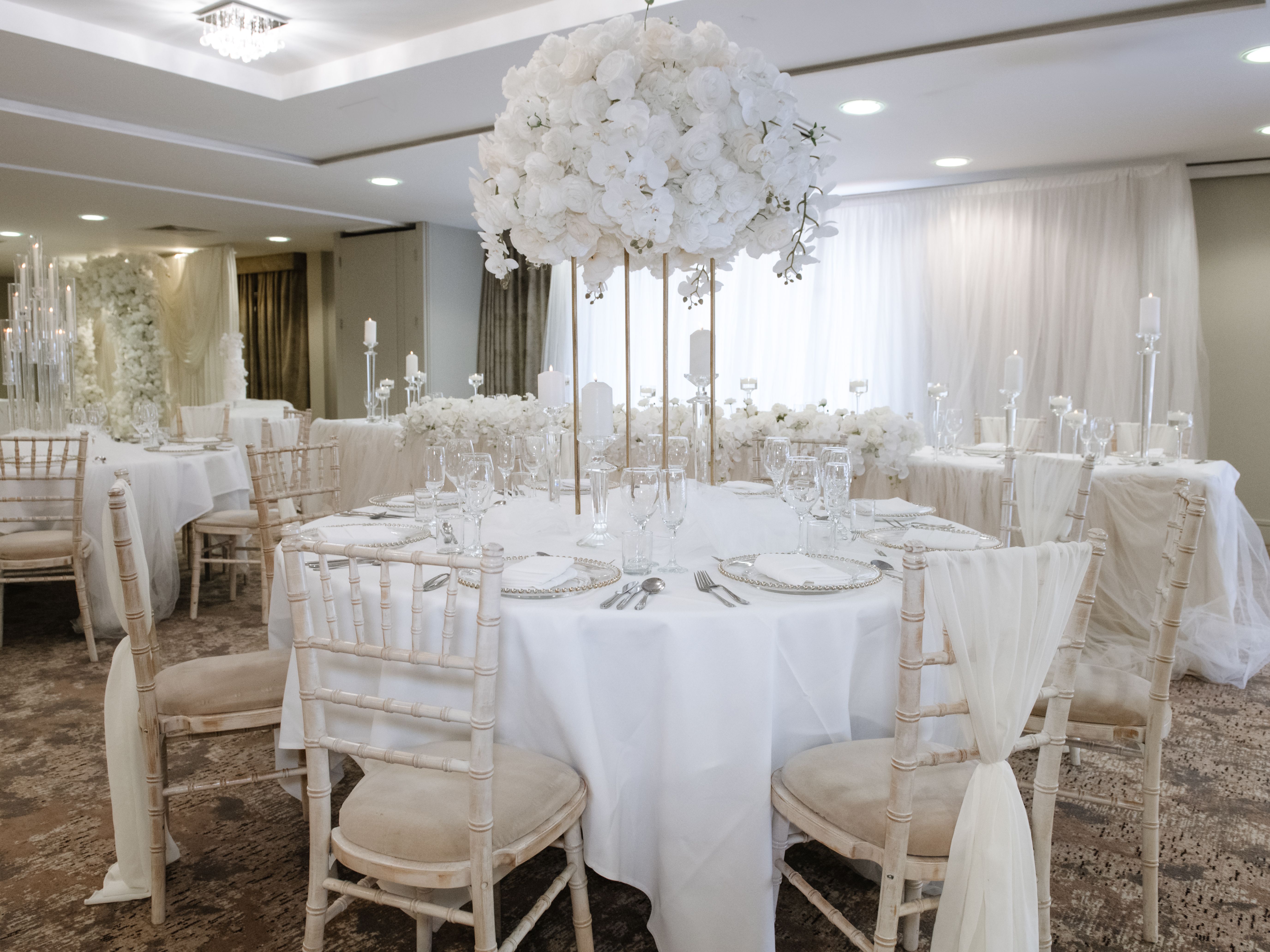 Elegant wedding reception hall with white floral centerpieces and draped chairs