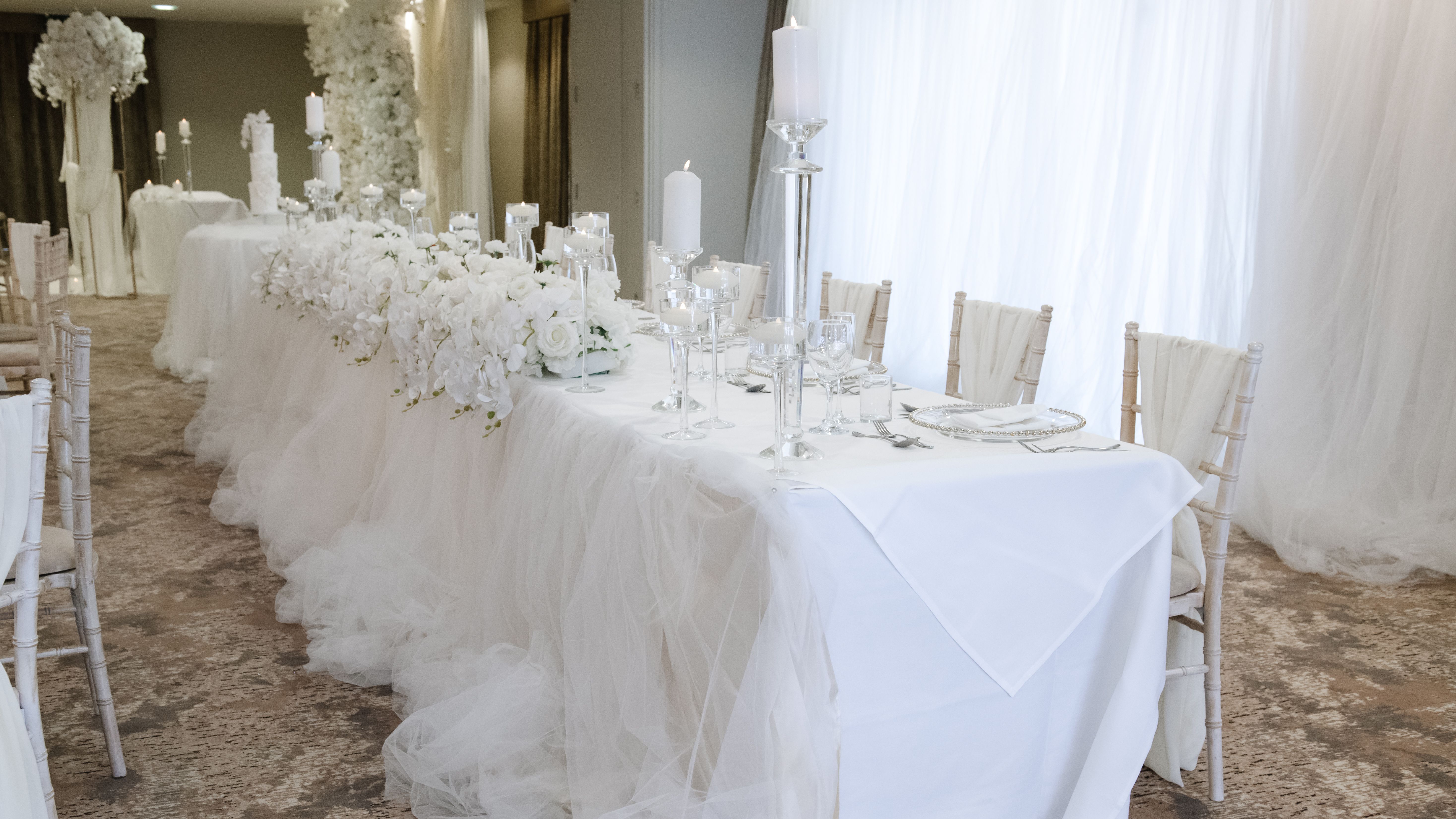 Elegant white wedding reception table setup with floral arrangements and candles.