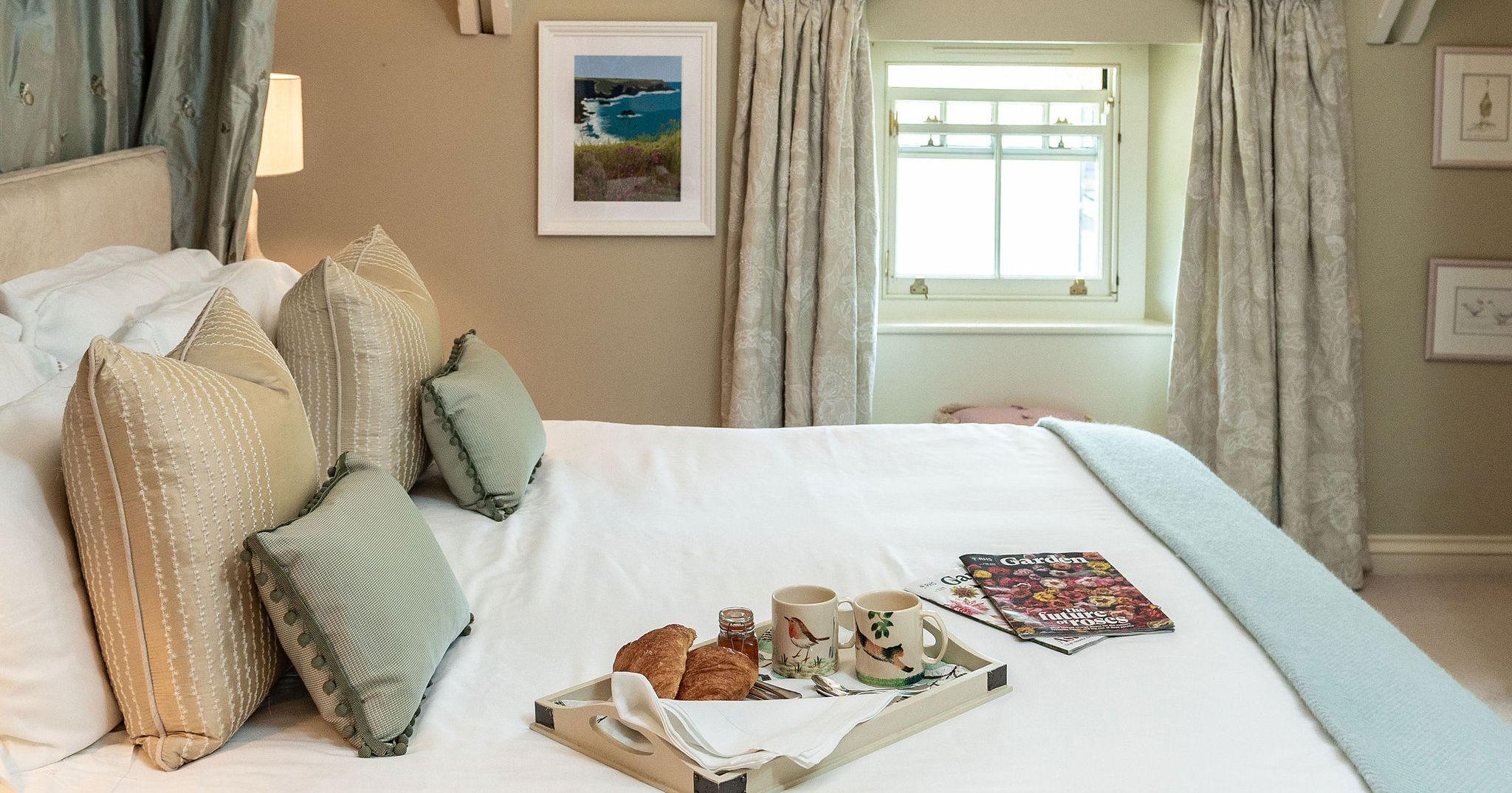 Bright and cozy bedroom with a tray of breakfast on the bed and magazines, featuring soft pillows and elegant decor.