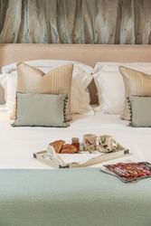 Breakfast tray with croissants, jam, and mugs on a neatly made bed with cushions and magazines