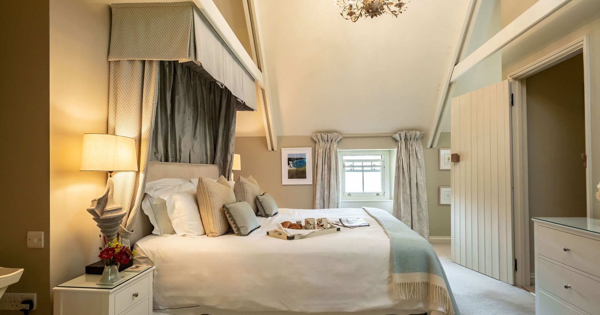 Elegant bedroom with vaulted ceiling, large bed, decorative chandelier, and cozy neutral decor.