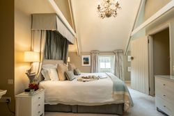 Elegant bedroom with vaulted ceiling, large bed, decorative chandelier, and cozy neutral decor.