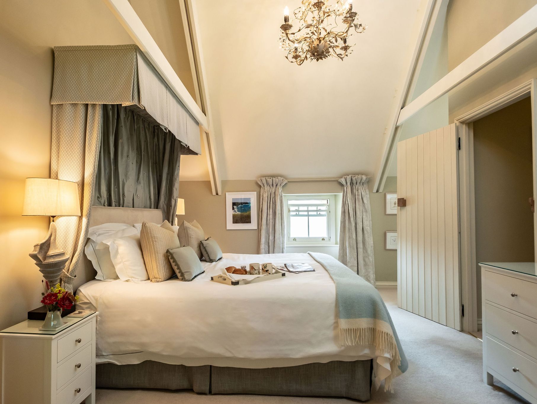 Elegant bedroom with vaulted ceiling, large bed, decorative chandelier, and cozy neutral decor.