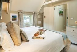 A cozy bedroom with a neatly made bed, decorative pillows, a breakfast tray with croissants and coffee, light curtains, and soft lighting.