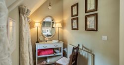 Cozy corner dressing table with an oval mirror, lamps, cushioned chair, and framed botanical art on pastel walls.