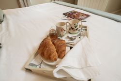 Breakfast tray with croissants, mugs, spoons, napkins, and a jar of jam on a bed