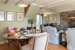 Cozy cottage living and dining area with stone fireplace, comfortable seating, and a set table with bread, cheese, and flowers.