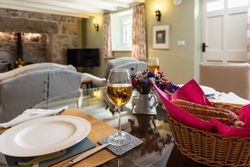 Table set for a meal with wine glasses, a basket of bread, and a cozy living room in the background.