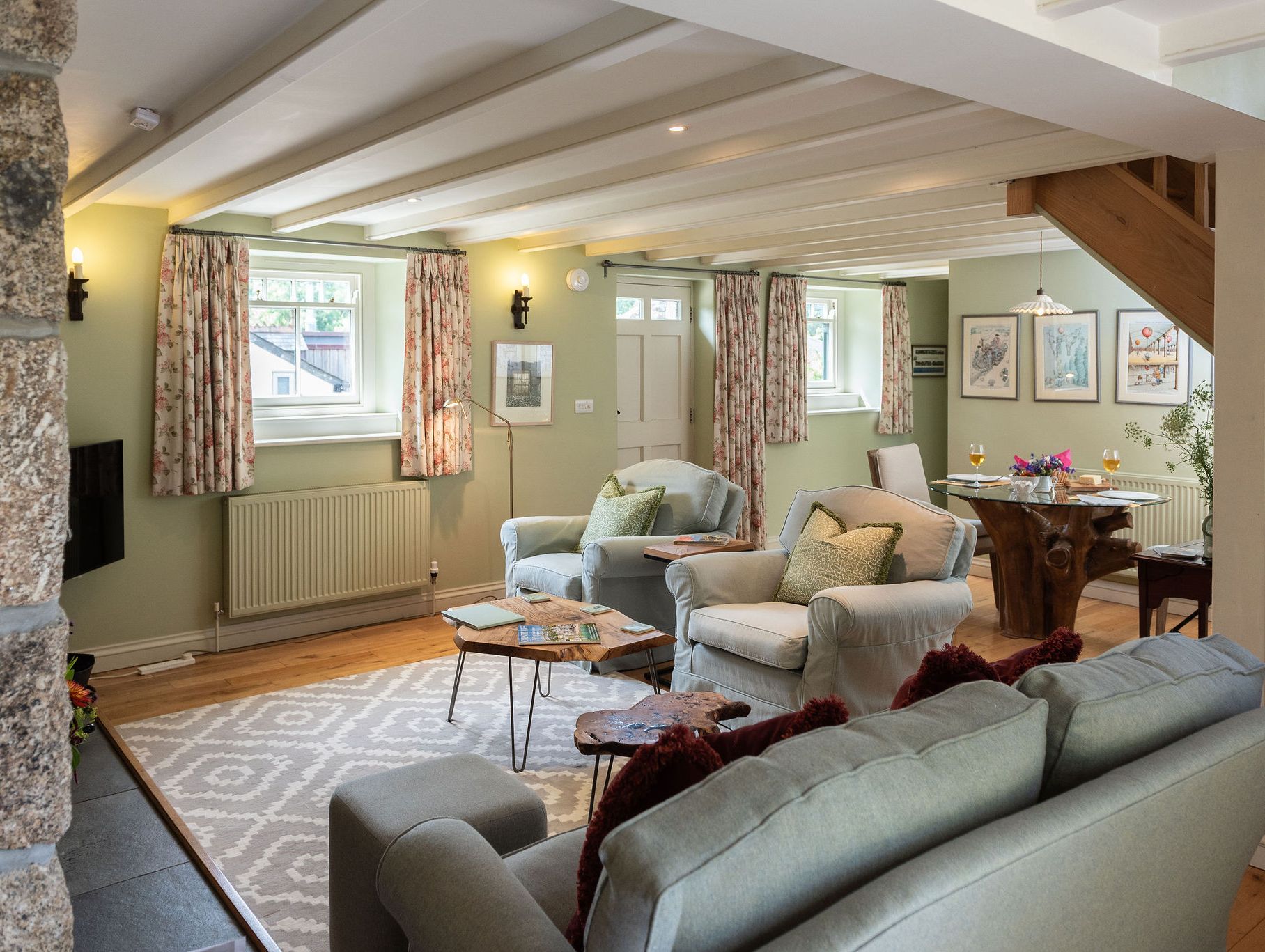 Cozy, stylish living room and dining area with pastel green walls, comfortable seating, and rustic wooden accents