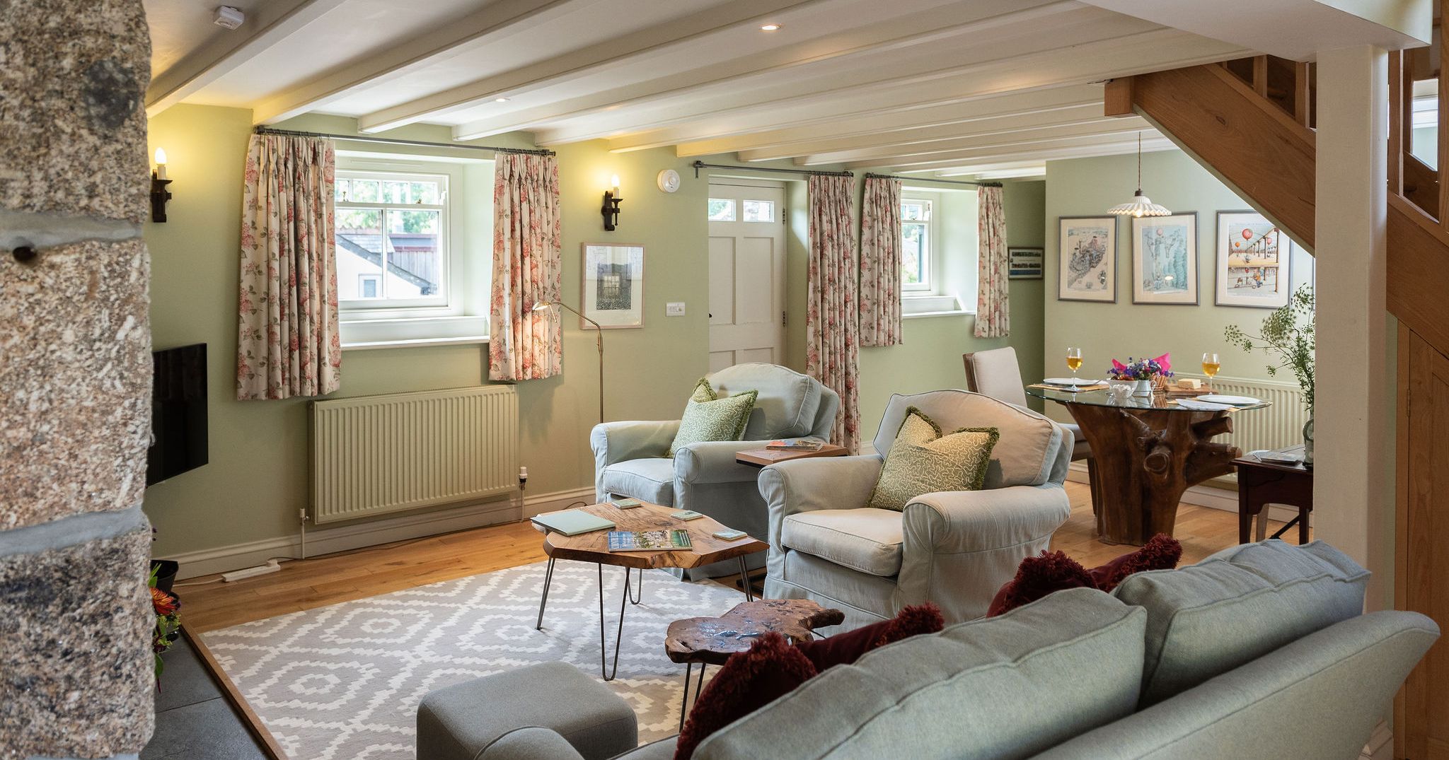 Cozy, stylish living room and dining area with pastel green walls, comfortable seating, and rustic wooden accents