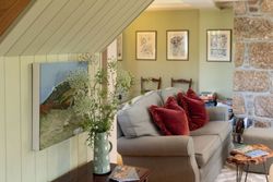 Cozy living room with a comfortable sofa, red cushions, framed artwork on the walls, and a vase of wildflowers on a wooden table.