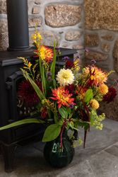 Colorful flower arrangement in a green vase placed next to a black wood-burning stove on a stone floor.