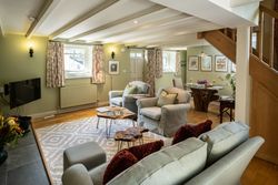 Cozy living room with light green walls, comfortable seating, floral curtains, wooden staircase, and a dining area.