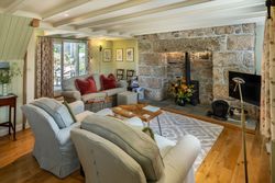 Cozy cottage living room with stone fireplace, wood-burning stove, comfortable armchairs, and a sofa with red pillows.