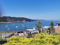 Boats anchored in Babbacombe Bay with coastal gardens and Cary Arms buildings in the foreground on a sunny day in South Devon