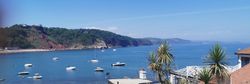 Boats anchored in Babbacombe Bay with coastal gardens and Cary Arms buildings in the foreground on a sunny day in South Devon