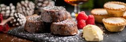 Christmas desserts with chocolate lava cakes, mince pies, raspberries, cream, and a glass of brandy with festive decorations in the background.
