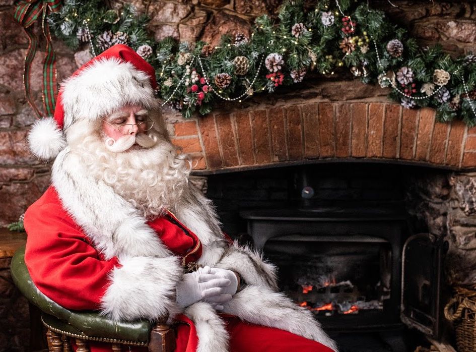 Santa Claus sitting by a fireplace decorated with Christmas garland