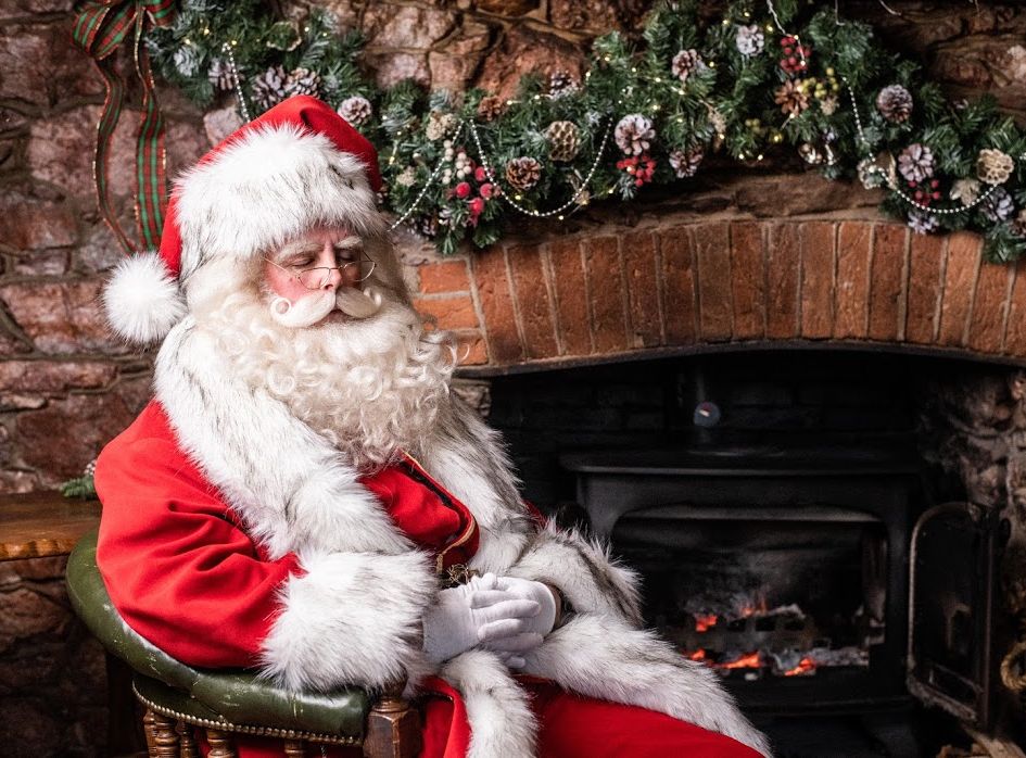 Santa Claus sitting by a fireplace decorated with Christmas garland