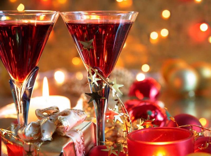 Two glasses of red wine surrounded by Christmas decorations and candles