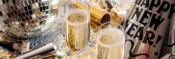 New Year's Eve party scene with two glasses of champagne, party hats, noise makers, gold and silver confetti, and a disco ball.