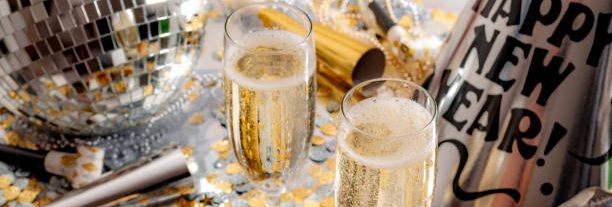 New Year's Eve party scene with two glasses of champagne, party hats, noise makers, gold and silver confetti, and a disco ball.