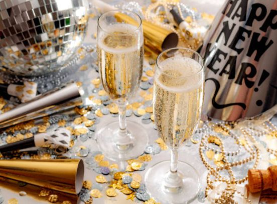 New Year's Eve party scene with two glasses of champagne, party hats, noise makers, gold and silver confetti, and a disco ball.