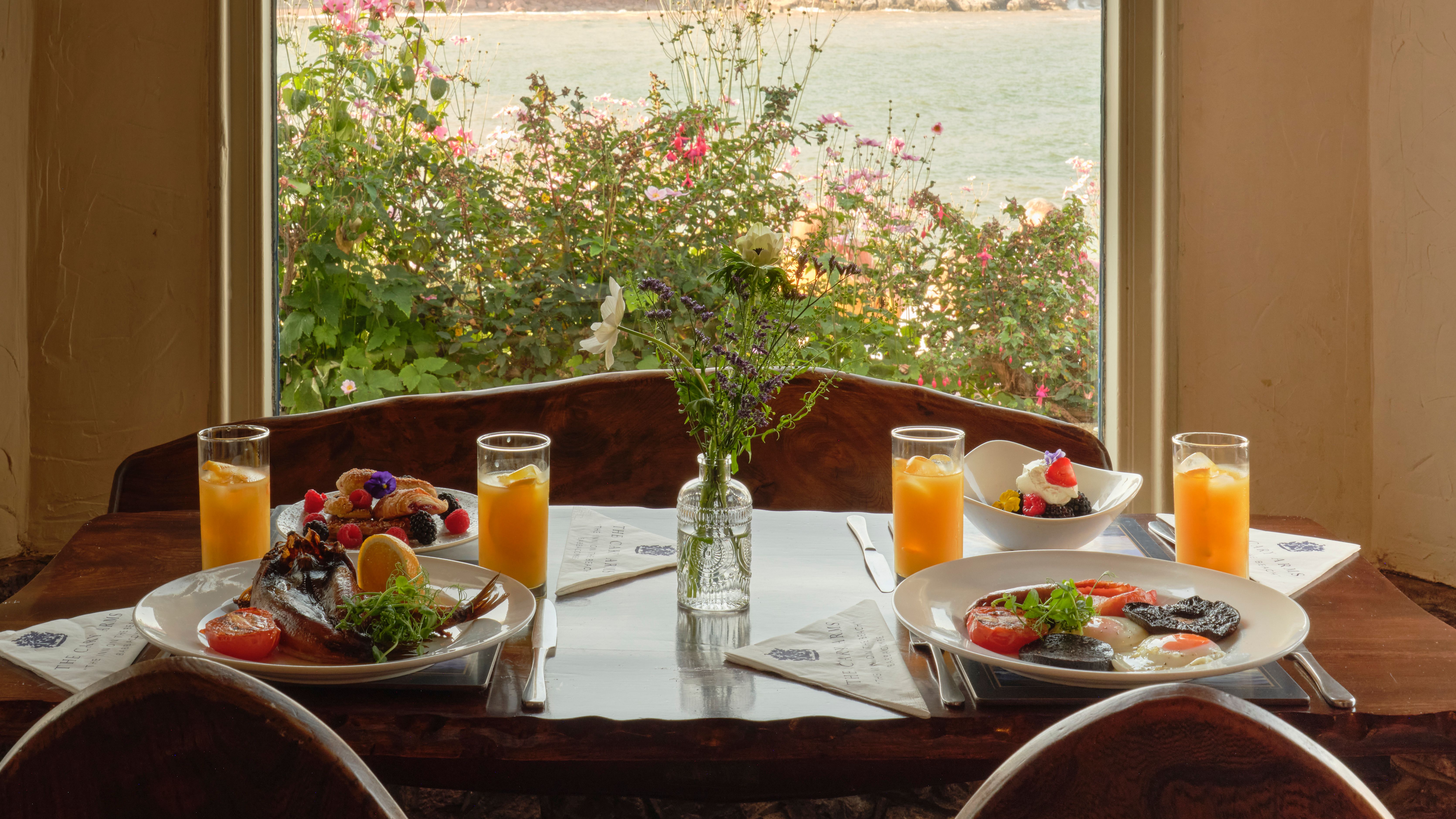 Breakfast table with plates of food and orange juice by a window overlooking the sea and cliffs