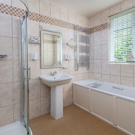Modern bathroom with tiled walls, glass shower enclosure, pedestal sink, bathtub, wall mirror, and window with blinds.