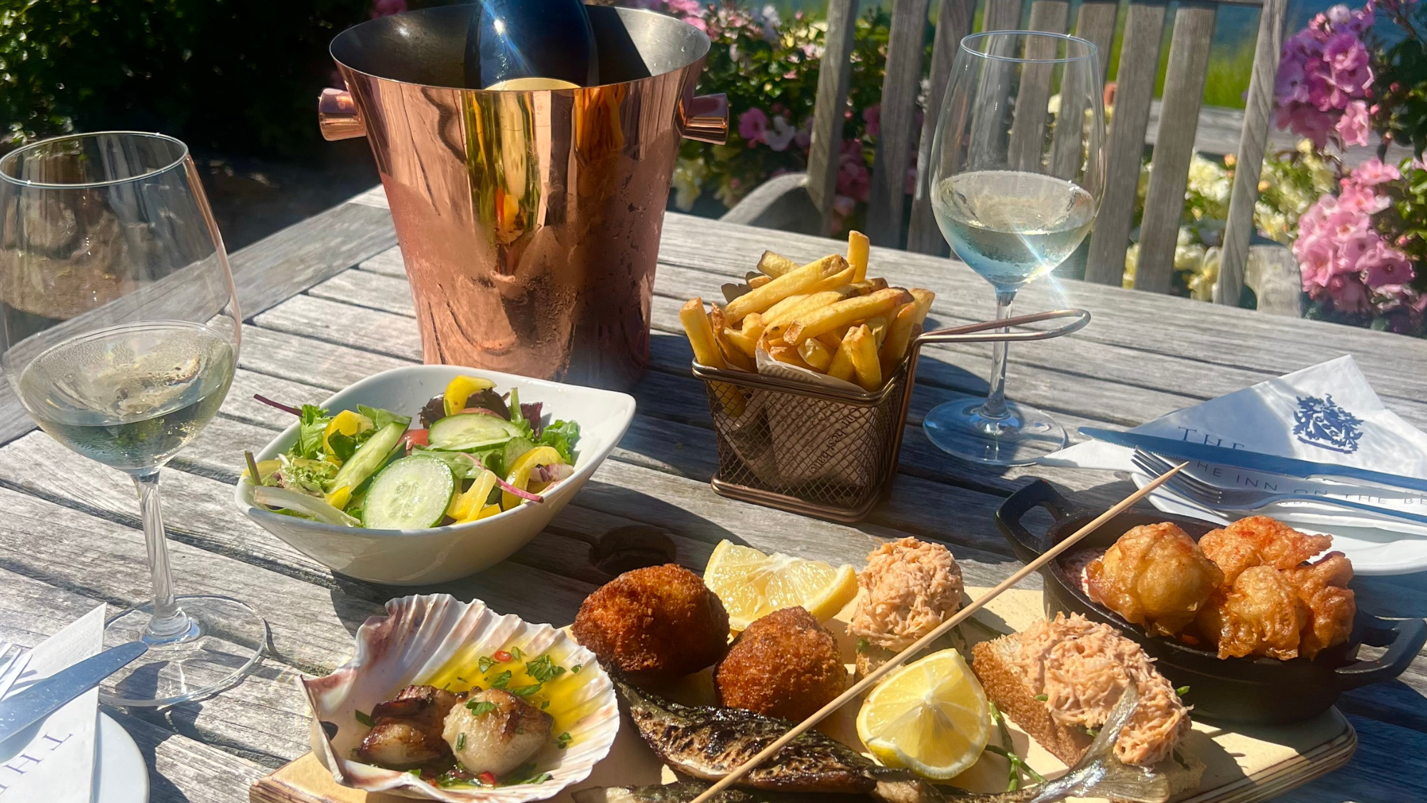 Outdoor table with wine, salad, fries, and assorted seafood tapas by the sea