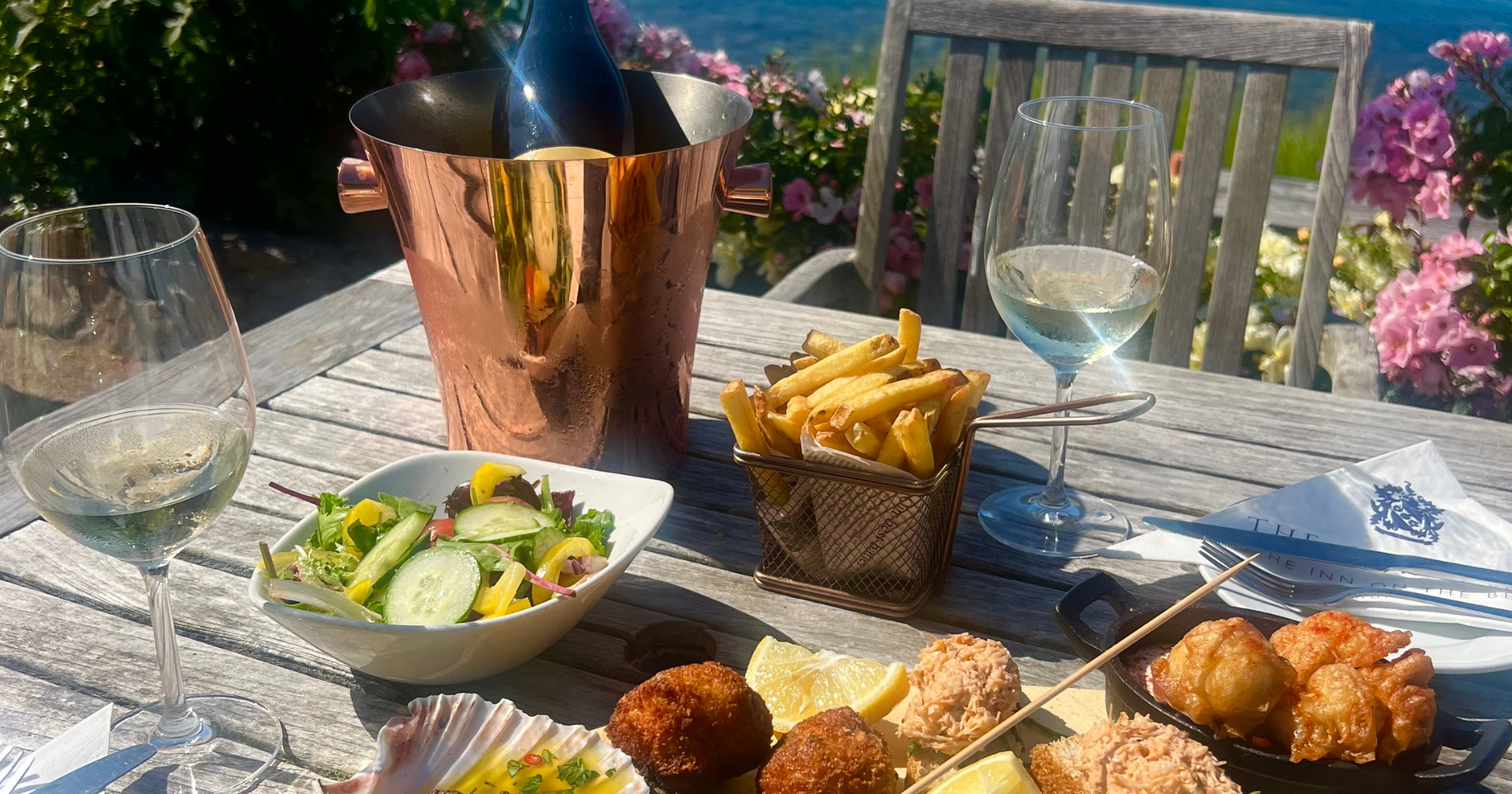 Outdoor table with wine, salad, fries, and assorted seafood tapas by the sea
