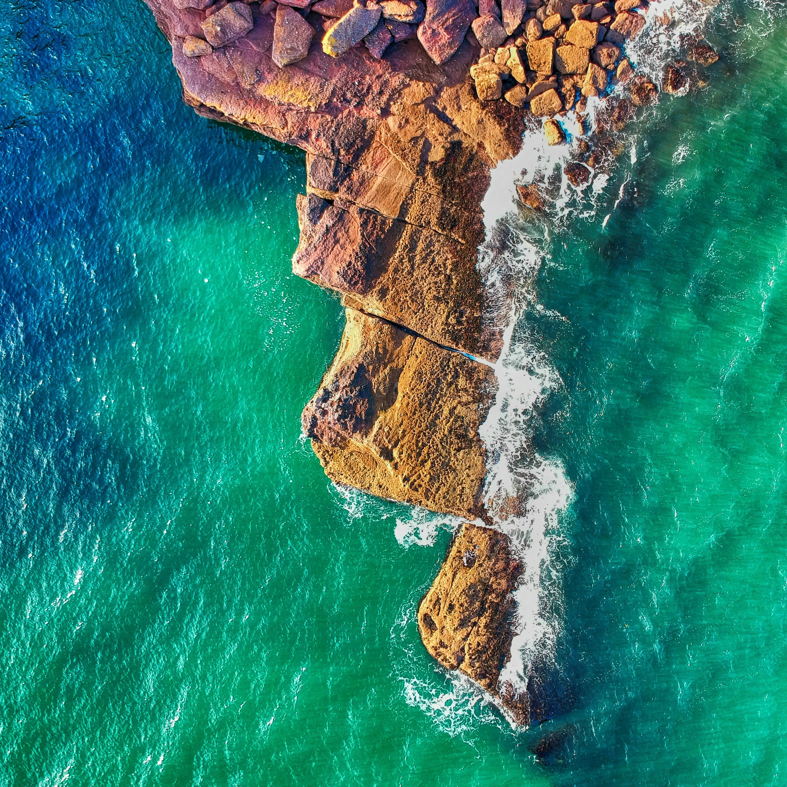 Aerial view of a rocky coastline with waves crashing against the rocks and turquoise water.