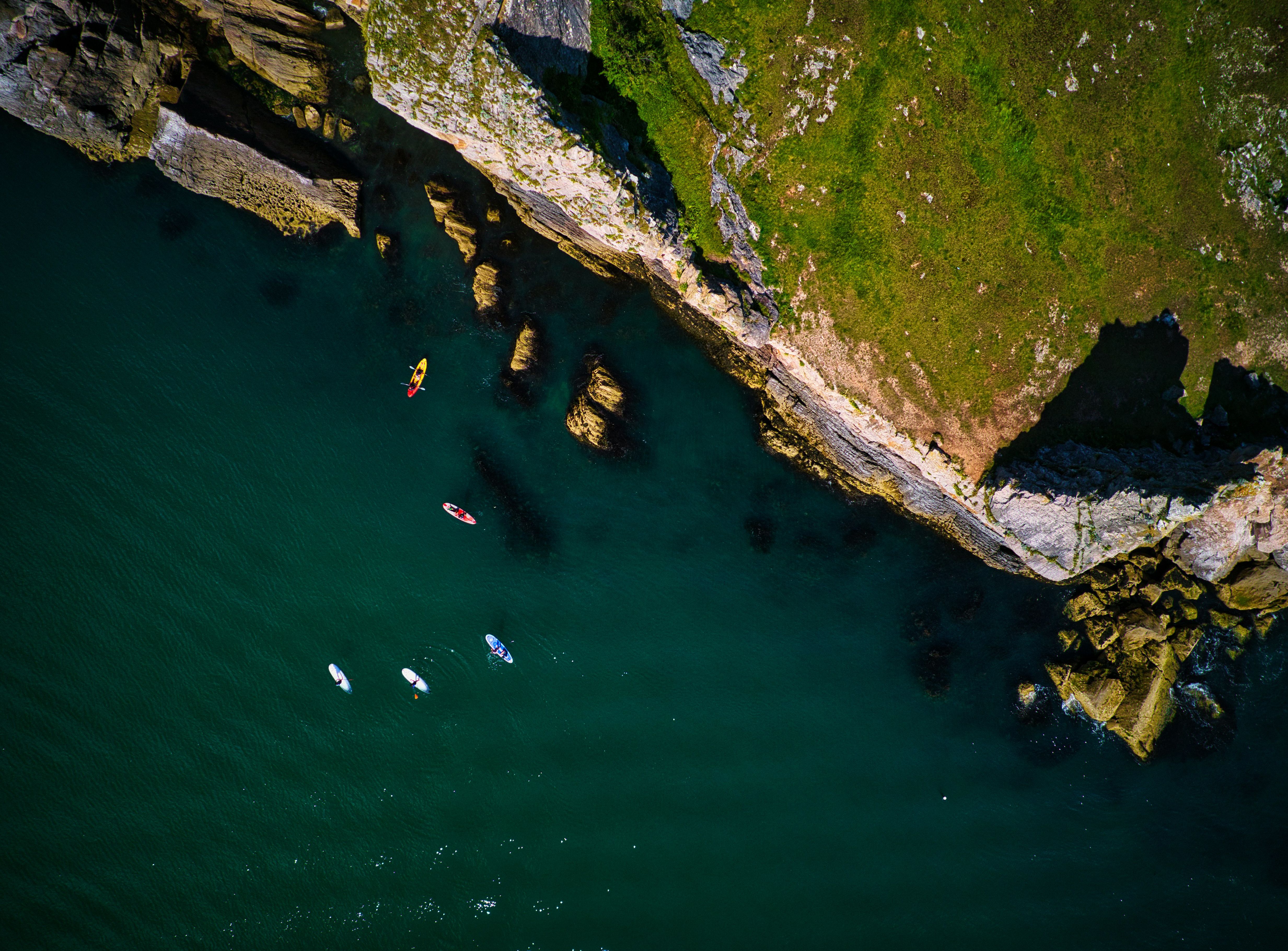 Aerial view of kayakers and paddleboarders near a rocky coastline with green grass above.